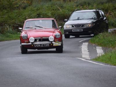 MGB GT 1972 rijd op een weg met een auto achter zich