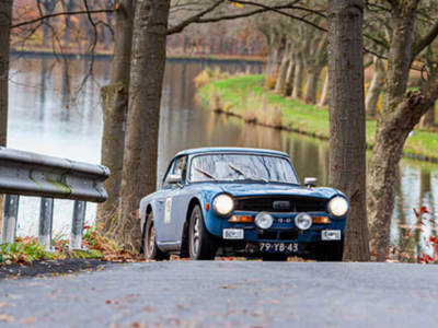 Triumph TR4  rijdt op een weg met een meer op de achtergrond